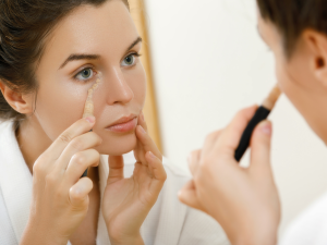 orretivo liquido e creme. Foto mulher branca passando corretivo abaixo dos olhos sobre o espelho