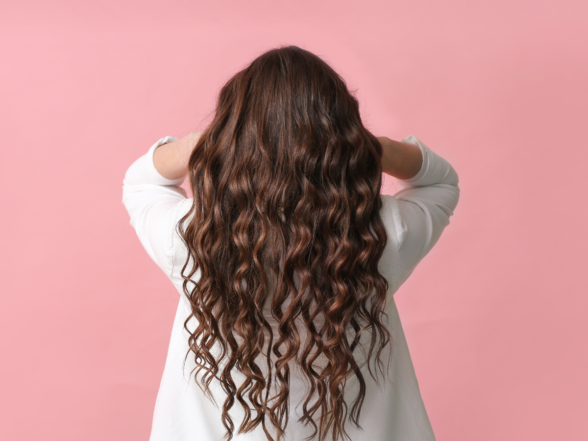 Cuidados essenciais cabelo ondulado. Foto mulher com cabelo ondulado comprido em um fundo rosa.