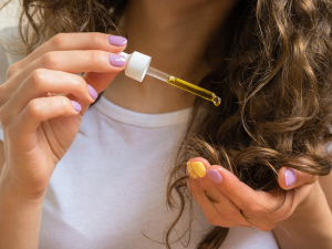 Umectação dos fios. Foto mulher passando óleo nas pontas dos cabelos com um conta gotas.