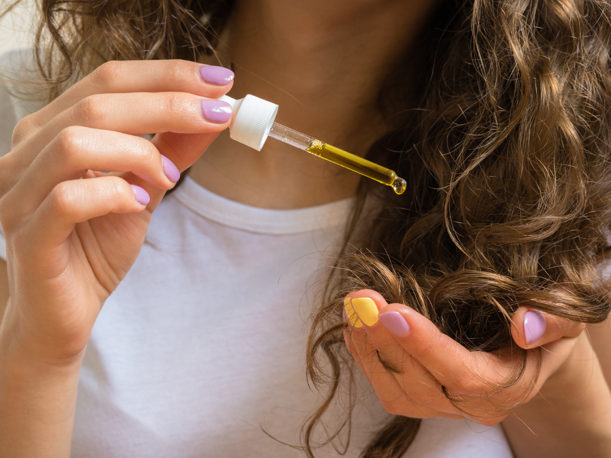 Umectação dos fios. Foto mulher passando óleo nas pontas dos cabelos com um conta gotas.