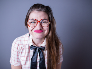 erros comuns na hora de se vestir. foto traz mulher branca com cabelo liso amarrado, cara de dor e camiseta xadrez branca com laranja e gravata em formato de laço na cor preta.